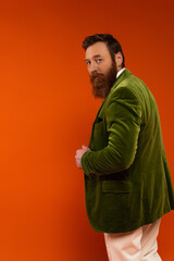 Stylish man in green velvet jacket looking at camera on red background.