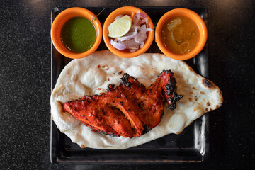 Tandoori chicken with naan in black plates on black table.