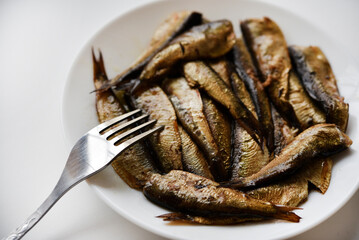 Canned fish on a white plate. Sprats and a fork. Fish in oil. Breakfast of fish.