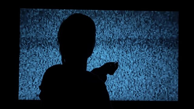 Silhouette of a girl watching TV with noises, shot from the back. Watching TV is a static glitch. Silhouette of a girl watching TV with static noise. Shot behind the shoulders of the model.