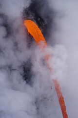 Lava stream falling from cliff surrounded by white cloud of steam, close up picture
