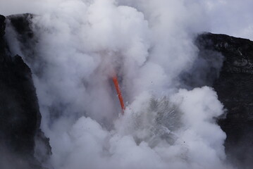 Lava falling out of cliff into the ocean surrounded by white cloud steam