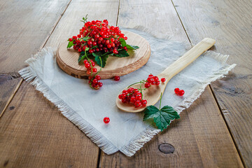 Red currants in a glass. On a wooden background, a light green napkin with leaves and red berries, on a napkin a glass transparent glass with red currant berries.