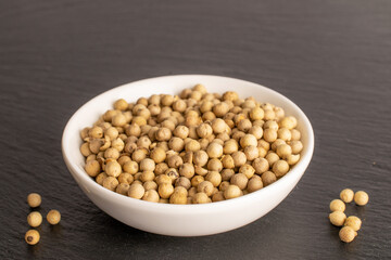 Fragrant vegetable coriander seeds in white plate on slate stone, macro.