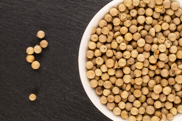 Fragrant vegetable coriander seeds in white plate on slate stone, macro, top view.