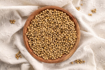 Fragrant vegetable coriander seeds with a wooden plate on a white linen napkin, macro, top view.