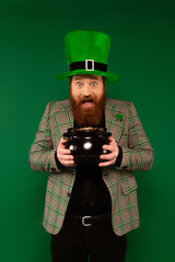 Bearded man in hat with clover holding pot with golden coins isolated on green.
