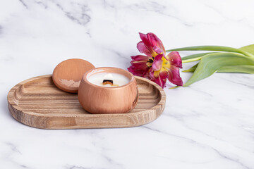 Interior candle in plaster candlestick and tulip on marble background. Candle on wooden tray