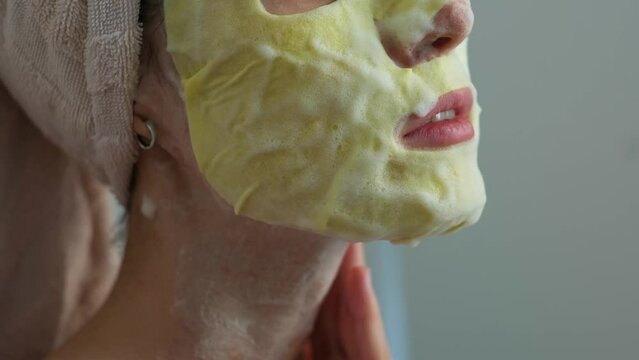 Close-up young woman applying cosmetic foam mask on her face in bathroom, skin care concept. 
