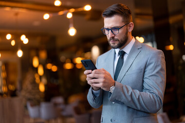 Serious worried businessman receiving unpleasant news on smartphone, reading e-mail or text message. Focused guy in business suit looking at mobile phone screen, typing or surfing the internet. - obrazy, fototapety, plakaty