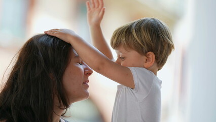 Naklejka premium Parenting stress. Patient mother. Little boy hitting parent in the head with hand. Child misbehavior outside. Lifestyle real life stressful moment