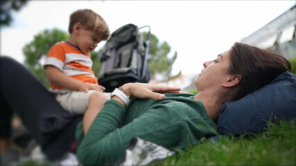 Mother laying on grass at park outdoors with child son enjoying weekend activity