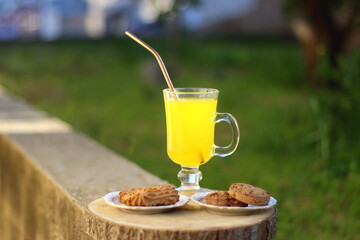 Glass of orange juice with reusable straw and two plates with cookies, served in a garden. Selective focus.