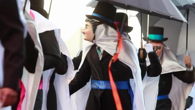 close up group of mexican male dancers during the Carnival in tlaxcala wearing a traditional costume with wooden mask and holding in one hand a black umbrella