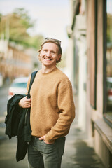 Outdoor portrait of handsome young man wearing beige fuzzy fleece sweater, posing on city street background