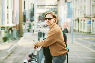 Outdoor portrait of handsome young man wearing sunglasses and beige fuzzy fleece sweater, posing on...