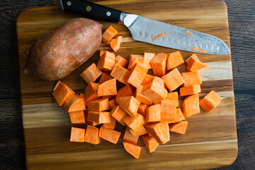 Peeled Sweet Potatoes Chopped Into Large Cubes: Prepped sweet potato chunks on a wooden cutting...