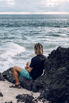  Young Caucasian, blond, sitting on the rocks watching the sea. Contemplation.