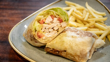 a tasty image of a freshly prepared chicken tortilla wrap filled with salad and served with French fries close up 