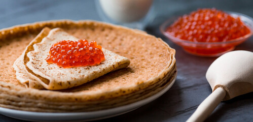 Russian traditions. Broad Maslenitsa. A stack of pancakes, sour cream and red caviar on a dark background. Close-up.