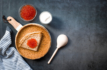 Russian traditions. Broad Maslenitsa. A stack of pancakes, sour cream and red caviar on a dark background. Close-up.