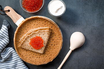 Russian traditions. Broad Maslenitsa. A stack of pancakes, sour cream and red caviar on a dark background. Close-up.