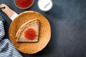 Russian traditions. Broad Maslenitsa. A stack of pancakes, sour cream and red caviar on a dark background. Close-up.