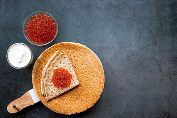 Russian traditions. Broad Maslenitsa. A stack of pancakes, sour cream and red caviar on a dark...