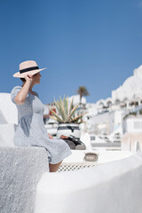 Tourist woman in blue dress with hat relaxing at sea view in the traditional village Thira. Walking Santorini tour, Greece, during her summer  crouise travel. European tourism attraction in Greece.