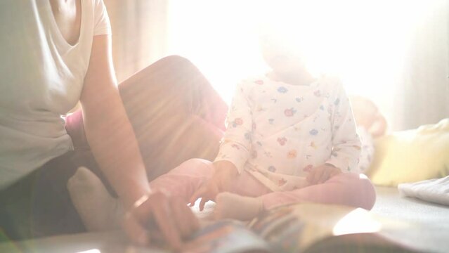 Mom reads a book to a little girl, running her finger along the lines