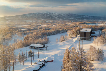 A panoramic view of the mountain and village in the snow with the golden ray of sunrise shining at the woods -- Niseko, Hokkaido, Japan  