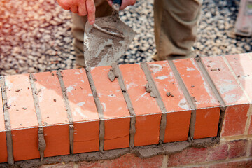 Close up of a brick wall and jointer trowel used by the worker to apply and level the mortar between bricks. Bricklayer making finishing touches to the brick wall and filling joints with mortar
