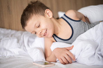 Obraz na płótnie Canvas beautiful cute 6 year old boy with smartphone in bed.