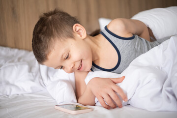 beautiful cute 6 year old boy with smartphone in bed.