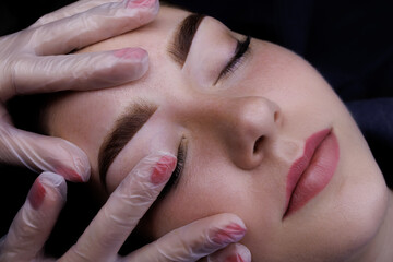 Permanent makeup of the eyebrows, the master touches the eyebrows of the model with his finger...