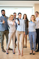 Full length of large group of confident business people showing thumbs up standing close to each other and smiling at office. Successful business team.