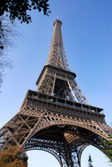 Closeup of the Eiffel tower of Paris in France among foliage on the blue sky background