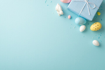 Easter decorations concept. Top view photo of blue giftbox with bow colorful eggs ceramic easter bunny and sprinkles on isolated pastel blue background with blank space