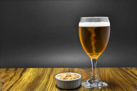 Vaso de Cerveza acompañado de Maní salado, servidos en una mesa. Espacio para texto al lado izquierdo.