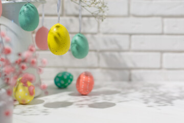 Closeup view of hanging fake eggs on table with brick wall with copy space. Decorated interior