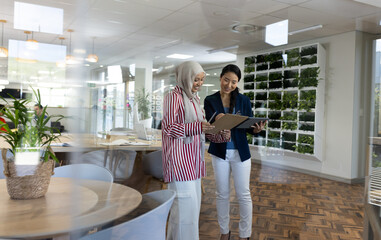 Happy diverse businesswomen with tablets talking in office lounge
