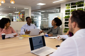 Diverse female and male businesspeople with laptops sitting at desk and talking