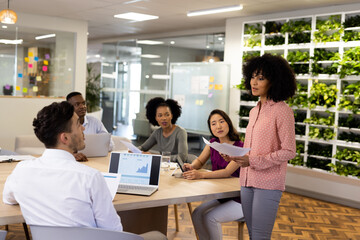 Diverse female and male businesspeople with laptops sitting at desk and talking