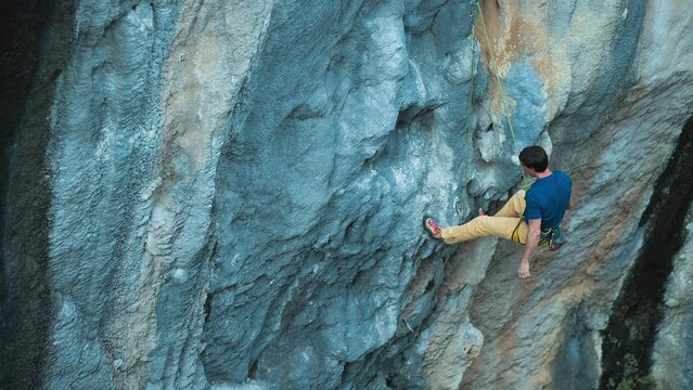 Strong rock climber lead climbing on overhanging rock face, rock climber making a big move, cinematic slow motion rock climbing