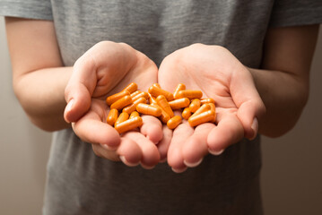 Woman hands hold handful of orange turmeric pills, healthy supplements, concept of wellness, selective focus close up shot