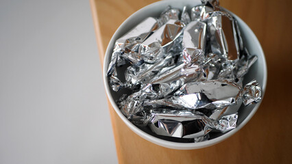 Candy wrapped in silver paper falling into a bowl - 572793453