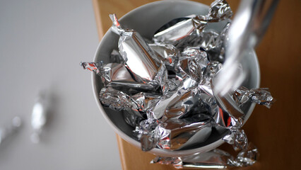 Candy wrapped in silver paper falling into a bowl - 572793459