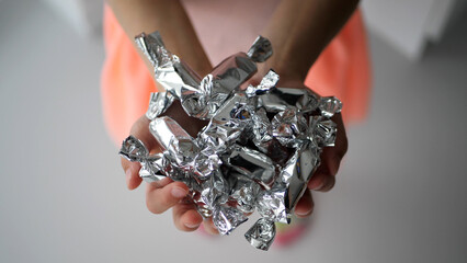 Close-up shot of a girl's hands holding a white ceramic bowl full of candy in silver wrapping paper - 572793467