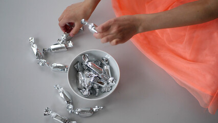 Girl putting silver candy into a ceramic bowl - 572793470