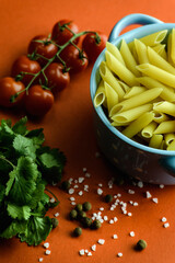 Top view of spices and vegetables, raw pasta in bowl on red background 